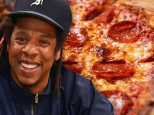 A man smiles in front of a pepperoni pizza.